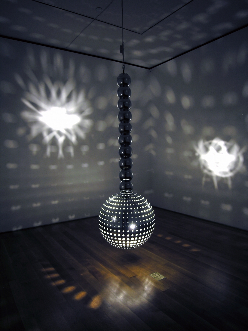 light sculpture suspended from the ceiling in a darkened gallery