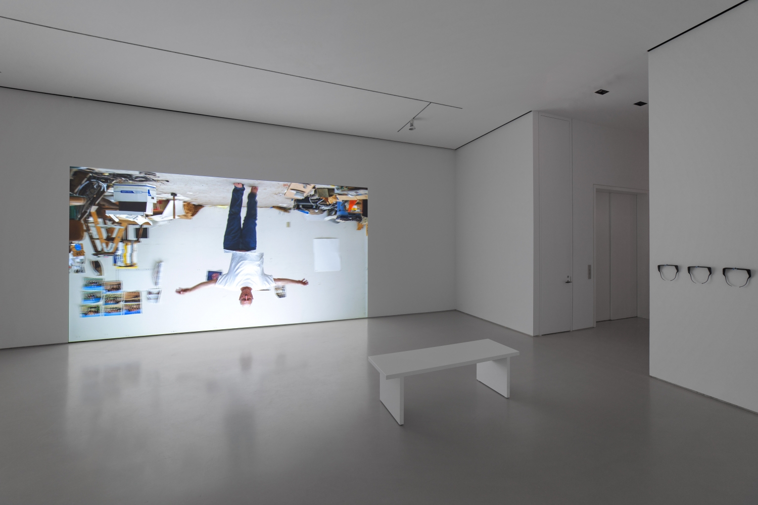 gallery installation view showing a projection of an upside down man walking with arms outstretched