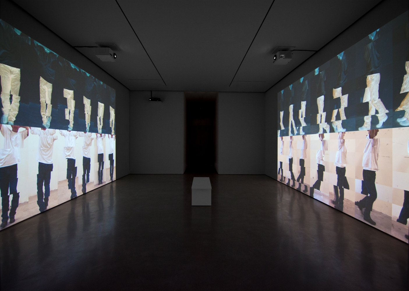 installation view of a darkened gallery with projections on opposite walls showing stacked rows of segmented man