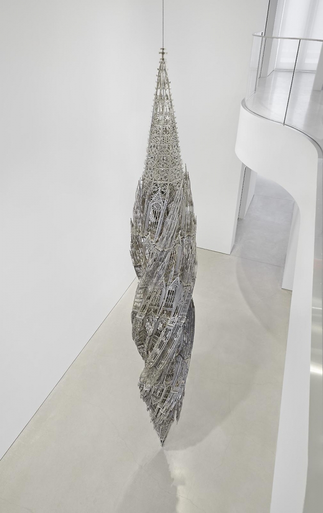 a large gothic spire mirrored vertically and twisted hangs in a large gallery